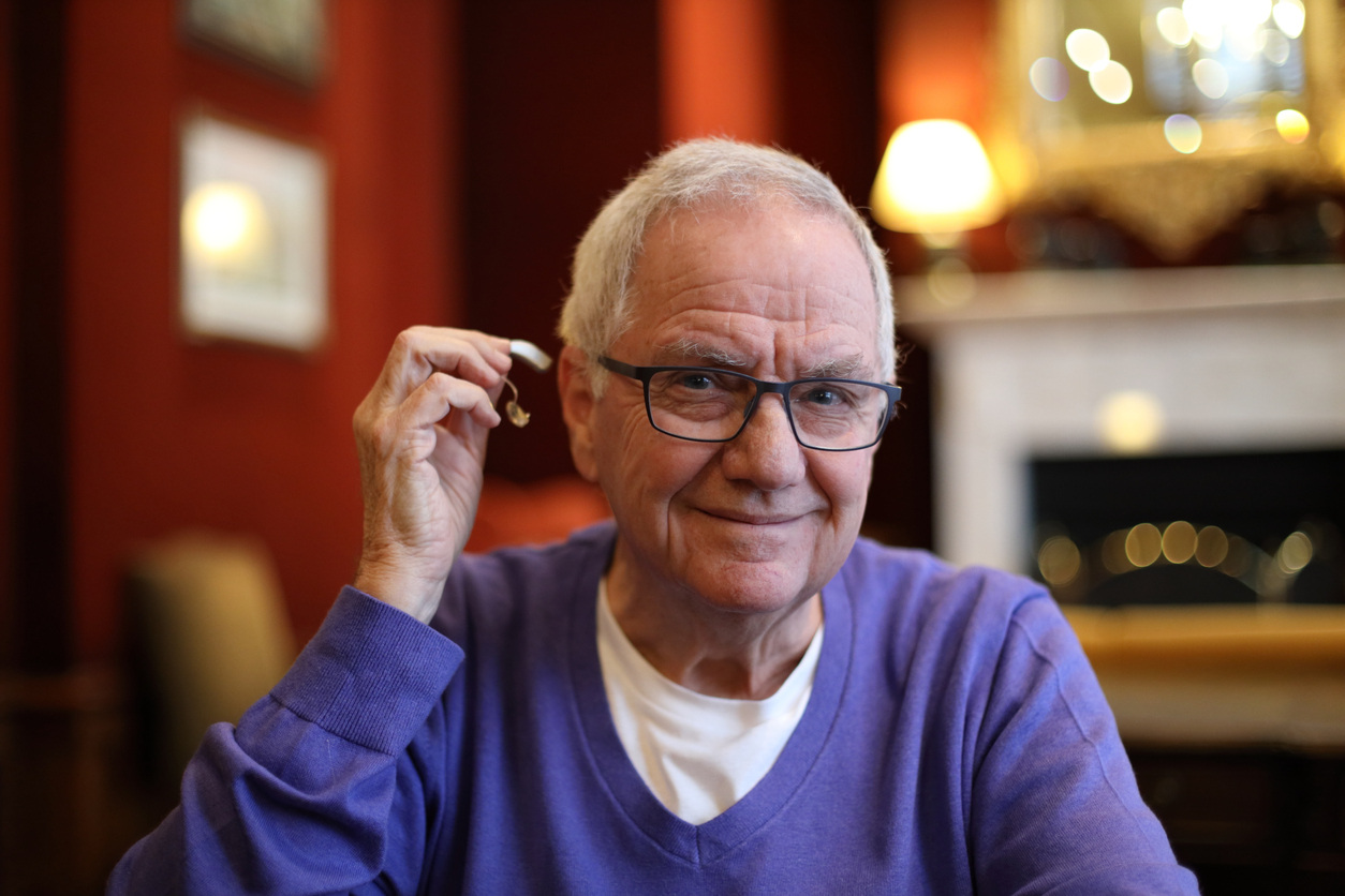 A person holds up their new hearing aid in a cozy living room.
